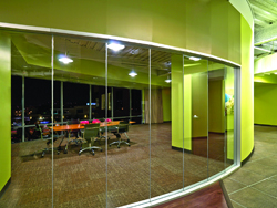 A glass-enclosed conference room with lime green walls, a long orange table, and several office chairs.