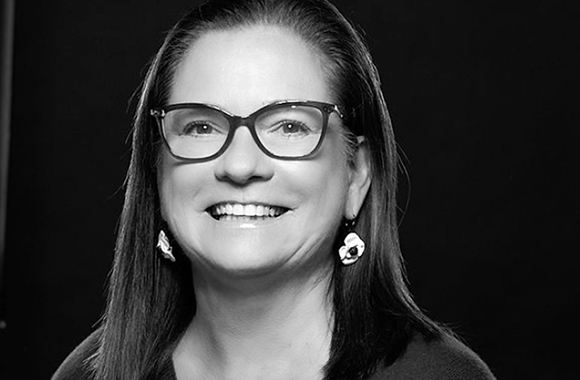 A smiling woman with long dark hair and glasses wearing decorative earrings.