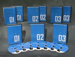 Six blue booklets numbered 01 to 03 and seven blue CDs arranged on a dark surface.