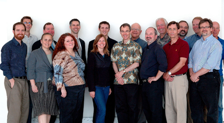 A group of approximately fifteen diverse men and women standing together in a professional group portrait.