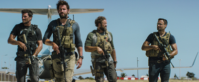 Four men in military tactical gear holding rifles standing outdoors in front of a small white airplane.