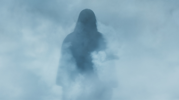 A dark silhouette of a person standing behind thick, swirling blue-tinted fog.