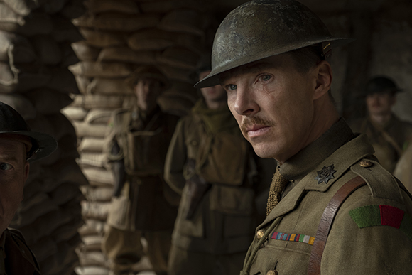 A soldier in a metal helmet and khaki uniform looks off-camera inside a sandbagged trench.