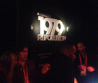 Illuminated sign displaying "1979 REVOLUTION" with people in the foreground.