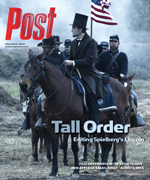 Man dressed as Abraham Lincoln on horseback with soldiers and an American flag.