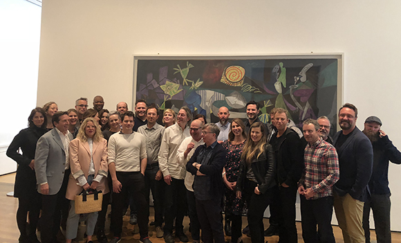 A group of people standing together in a museum in front of a large, colorful abstract painting.