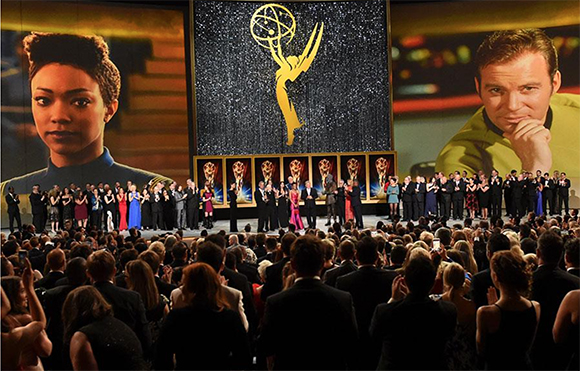 A large stage with a gold trophy emblem and two large portraits of people flanking a group of people.