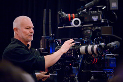 A man in a black shirt adjusts a large professional cinema camera on a tripod.
