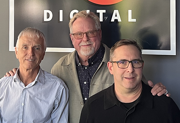 Three men standing together in front of a black sign with the word DIGITAL in white letters.