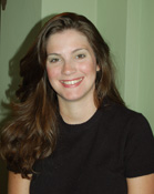 A smiling woman with long brown hair wearing a black t-shirt against a light green background.