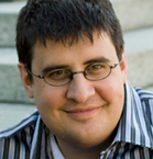 A man with short dark hair and glasses smiling at the camera.