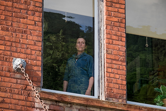 A woman in a blue shirt looks out of a window of a red brick building.