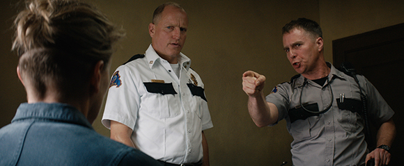 Two male officers in uniform confront a person from behind in a dimly lit room.