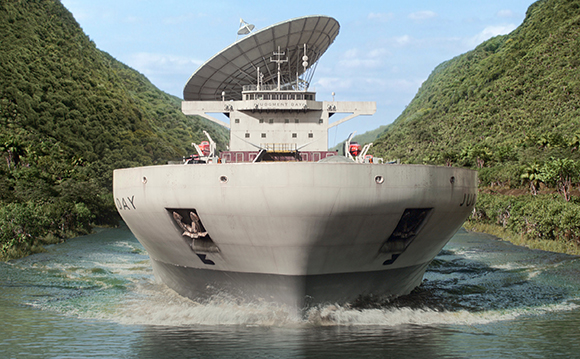 A large white ship with a massive satellite dish on its deck moves through a narrow, lush green canal.