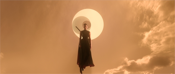 A silhouette of a person standing before a large white circle in a golden, cloudy sky.