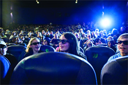 A crowd of people sitting in theater seats wearing sunglasses in a dimly lit room.