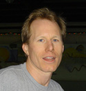 A man with short light brown hair and a grey t-shirt looking forward.