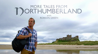 Robson Green stands on a beach with a backpack, with a castle on a hill in the background under a cloudy sky.