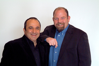 Two smiling men in blazers posing together against a white background.