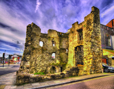 Stone ruins of a weathered, multi-story building under a dramatic purple and blue cloudy sky.