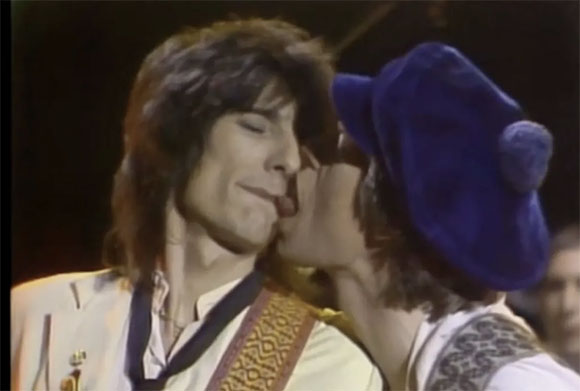 A person in a blue hat kisses another person on the cheek.