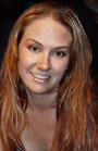 A smiling woman with long, wavy blonde hair looking toward the camera.