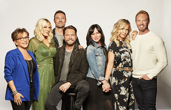 Seven smiling people of various ages posing together against a white background.