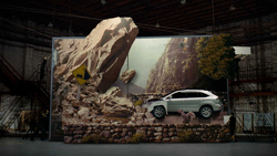 A large advertisement showing a white SUV driving through a rocky mountain landscape in a warehouse setting.