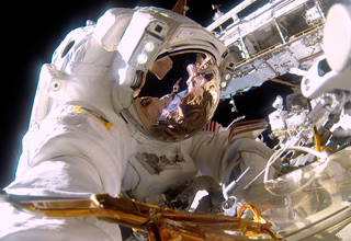 Close-up of an astronaut in a white spacesuit with a reflective gold visor in space.