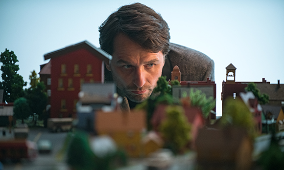 A man leans in closely to observe a detailed miniature model of a small town.