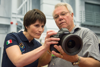 A woman in a navy polo shirt and a man in a grey shirt examine a black Canon DSLR camera together.