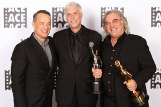 Three men in dark suits smiling and holding two golden awards in front of an ACE logo backdrop.