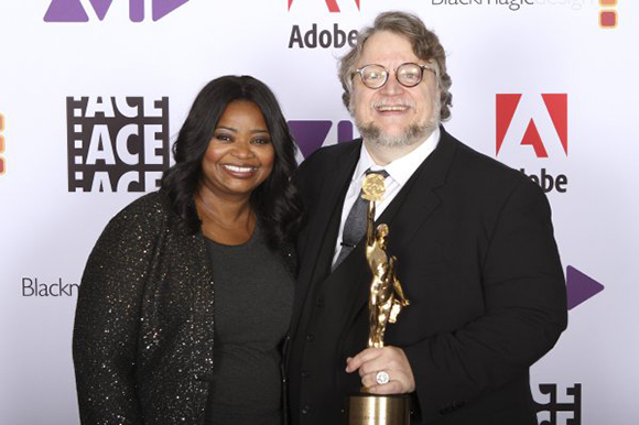 A woman in a black sparkly jacket and a man in a suit holding a gold award trophy.