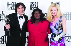 Three people in formal attire pose together, holding awards in front of an ACE backdrop.