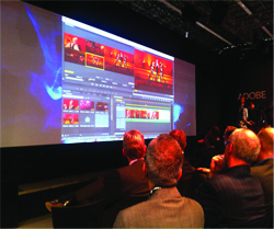 Audience watches a large screen displaying Adobe Premiere Pro video editing software with multiple video clips and timelines