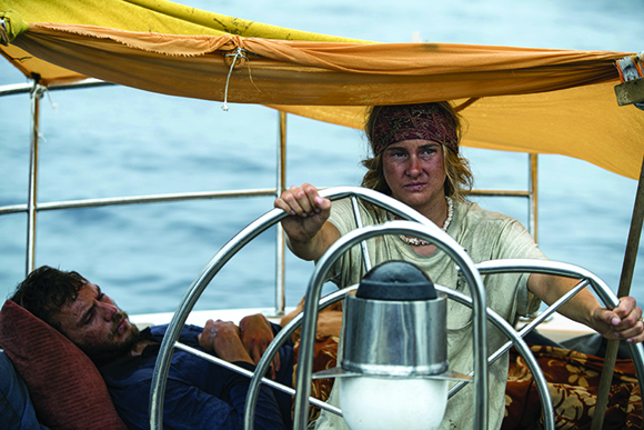A person with a headband steers a boat under a yellow canopy while another person rests nearby.