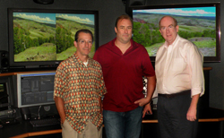 Three men pose in a studio in front of large screens showing green hills and landscapes.