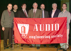 Six men stand in a row behind a red banner that reads 'AUDIO ENGINEERING SOCIETY'.