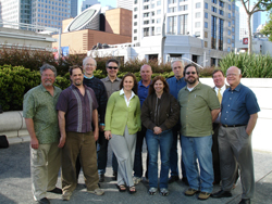 A group of eleven diverse adults standing together for a group portrait in an urban outdoor setting.