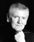Black and white portrait of a man with short hair resting his chin on his hand against a dark background.
