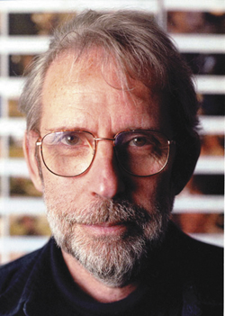 Close-up portrait of an older man with graying hair, glasses, and a salt-and-pepper beard.