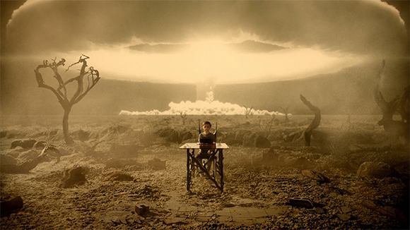 A person sits at a desk in a barren, rocky wasteland under a massive, glowing cloud formation.