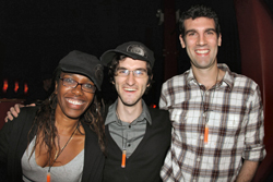 Three smiling people posing together in a dark setting.