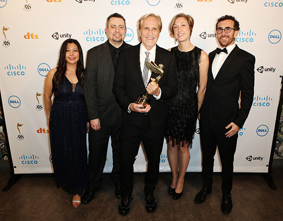 Five people in formal attire pose in front of a white backdrop with corporate logos.