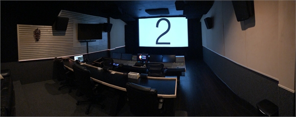 A dark control room with a long desk, computer monitors, and a large screen showing the number 2.