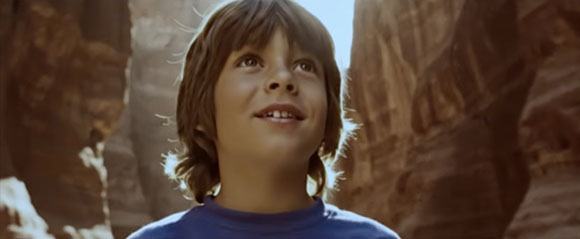 A young boy with brown hair looks up with a smile against a backdrop of canyon walls.