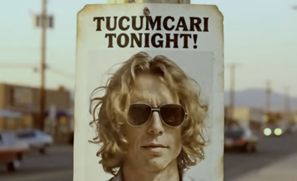 A weathered sign with the text 'TUCUMCARI TONIGHT!' above a portrait of a man with wavy hair and sunglasses.