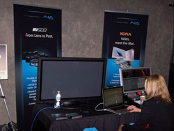 A person sits at a desk with a laptop and monitor in front of two large promotional banners.