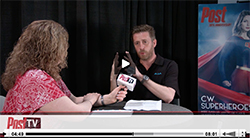 A man in a black shirt speaks to a woman in a red patterned shirt during an interview.