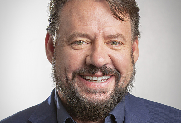 A smiling man with brown hair, light eyes, and a salt-and-pepper beard wearing a blue blazer.